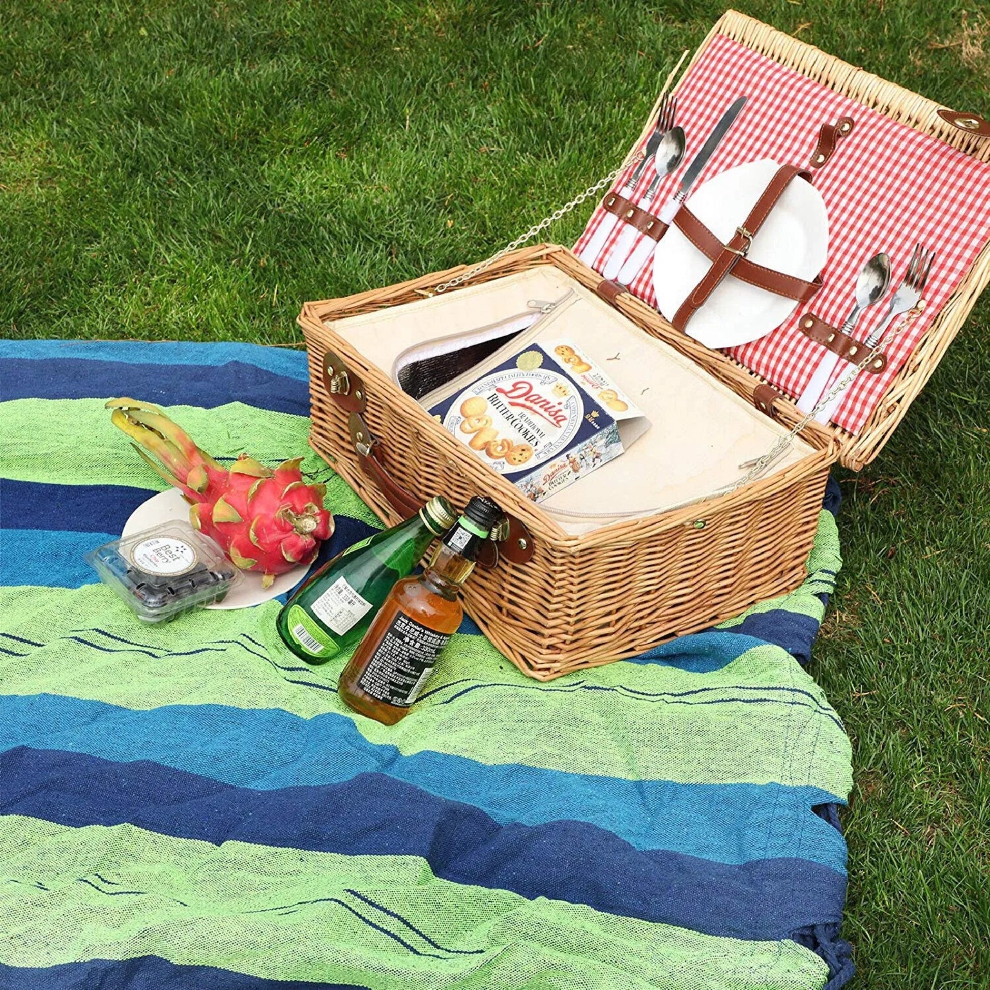Open picnic basket with food and drinks on a striped blanket outdoors